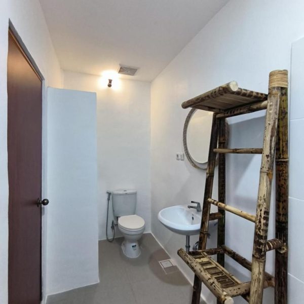 Baño moderno con decoración de bambú, lavabo, inodoro y espejo circular en Roots Hotel Senggigi