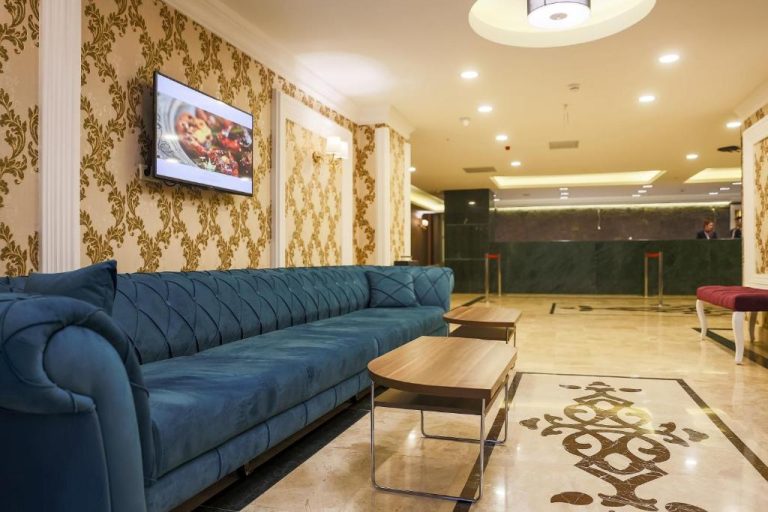 Elegante lobby del Royal Hotel Inegol con sofá azul de terciopelo y recepción de mármol verde