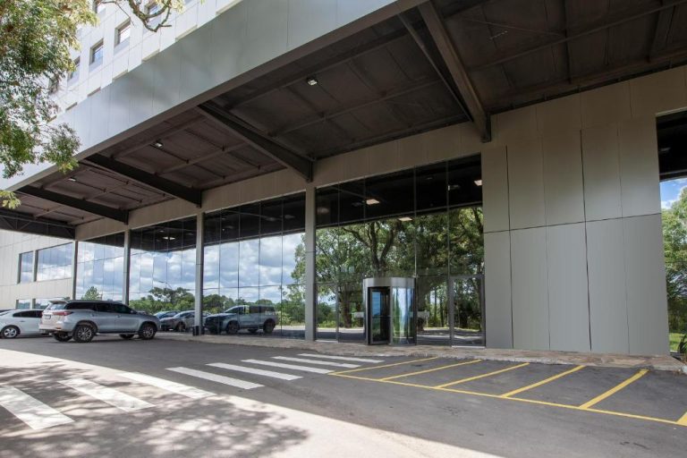 Entrada principal con acceso en vidrio y estacionamiento del Tri Hotel Antônio Prado