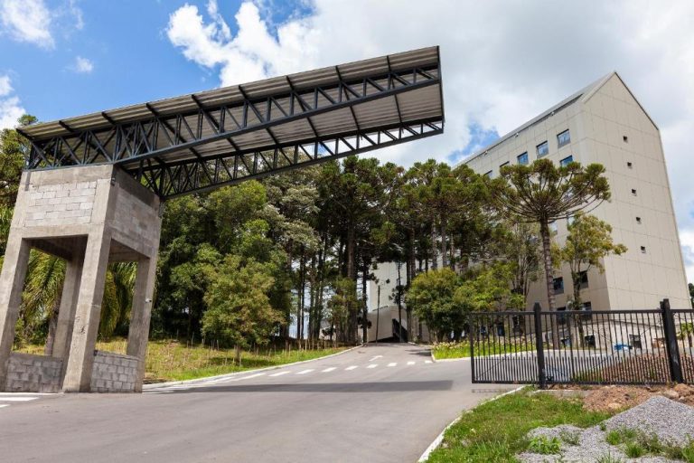 Entrada principal del Tri Hotel Antônio Prado con pórtico metálico y edificio moderno rodeado de árboles