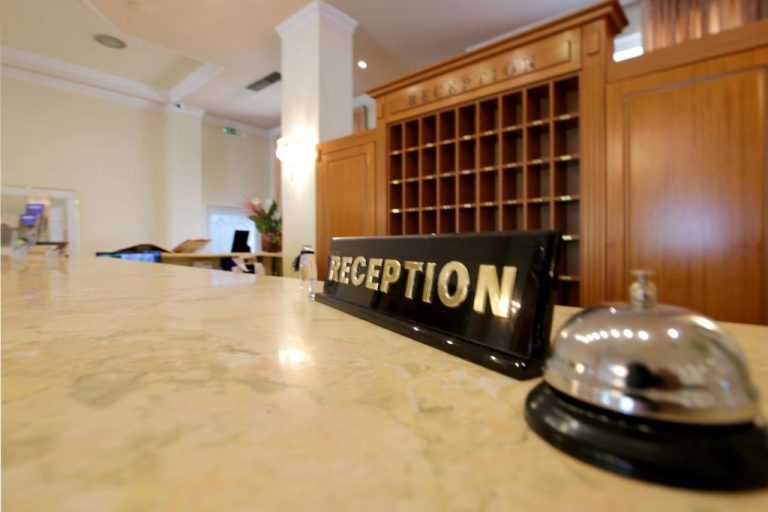 Mostrador de recepción con timbre y estantería de madera clásica en el Hotel Philippos Livadeia