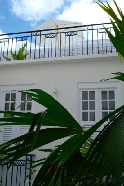 Fachada blanca con balcón de hierro forjado y palmeras tropicales del Maison Victoire Boutique Hôtel en Pointe-à-Pitre