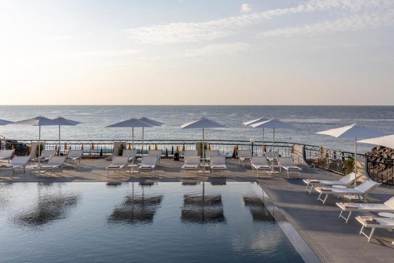 Piscina infinita con tumbonas y sombrillas blancas frente al mar en Delta Hotels by Marriott Giardini Naxos