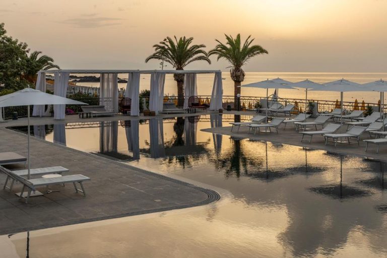 Piscina infinita con tumbonas y vistas al mar al atardecer en Delta Hotels by Marriott Giardini Naxos