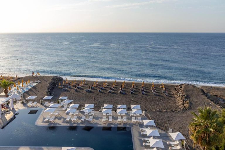 Piscina infinita con tumbonas y playa de arena volcánica del Delta Hotels by Marriott Giardini Naxos