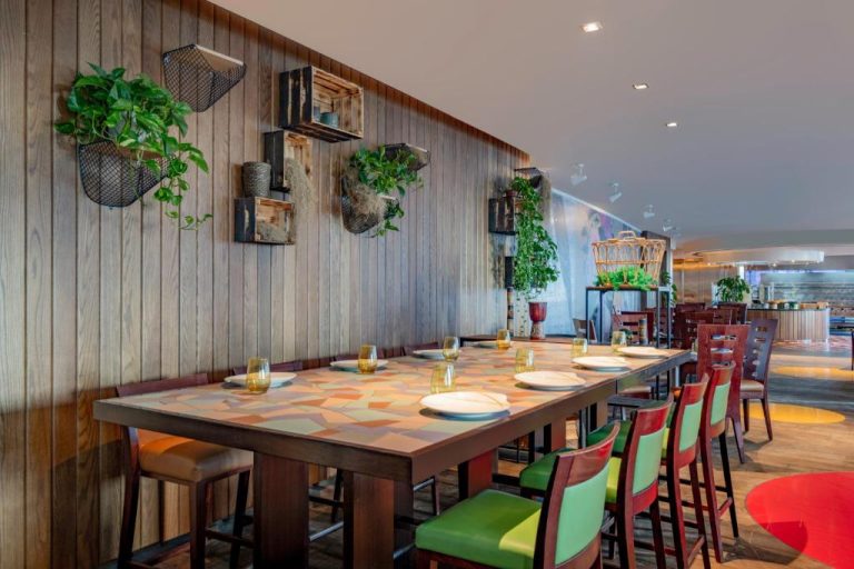 Restaurante interior del Marriott Marquis City Center Doha con mesas de madera, sillas coloridas y plantas decorativas