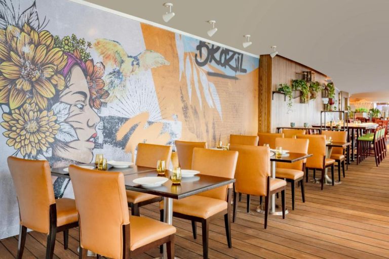Restaurante del Marriott Marquis Doha con mural artístico urbano y mesas con sillas de cuero naranja