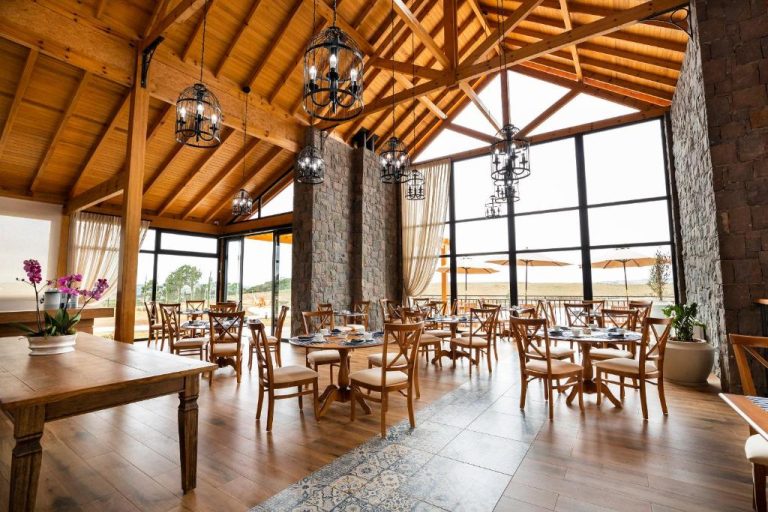 Restaurante interior con techo de madera y vigas, mesas de madera y grandes ventanales en Cerro Azul Hotel Fazenda