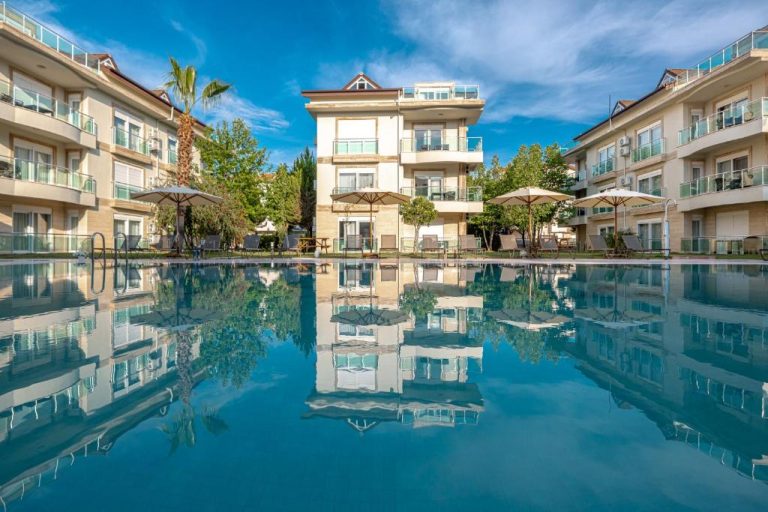 Piscina exterior con reflejo del edificio principal del Belek Deluxe Suit rodeada de sombrillas