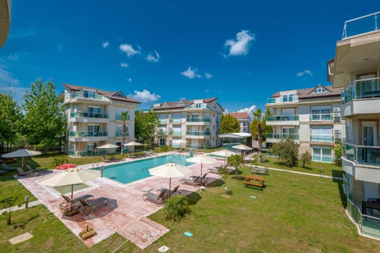 Piscina exterior con tumbonas y sombrillas rodeada de jardín en Belek Deluxe Suit