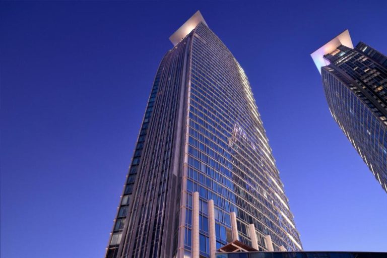 Vista exterior de la torre de cristal del hotel Le Meridien City Center Doha bajo un cielo azul