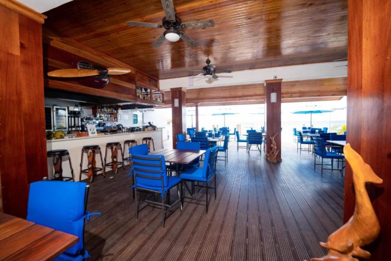 Restaurante y bar con sillas azules y terraza con vistas al mar en Blue Skies Beach Resort