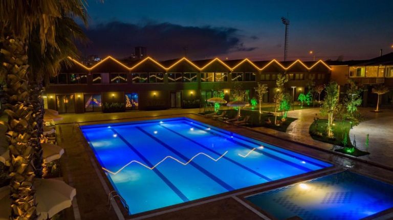 Piscina exterior iluminada de noche en el Green Palace Suite Hotel con luces LED azules y decoración