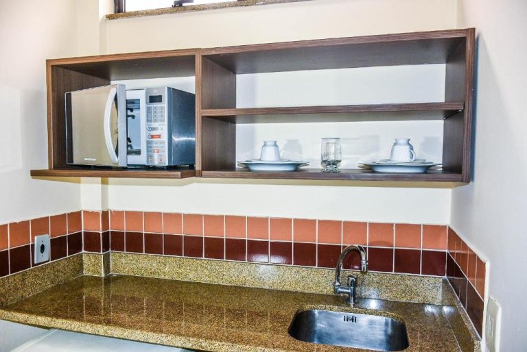 Cocina equipada con microondas, fregadero y estantes con vajilla en Mont Blanc Apart Hotel Nova Iguaçu