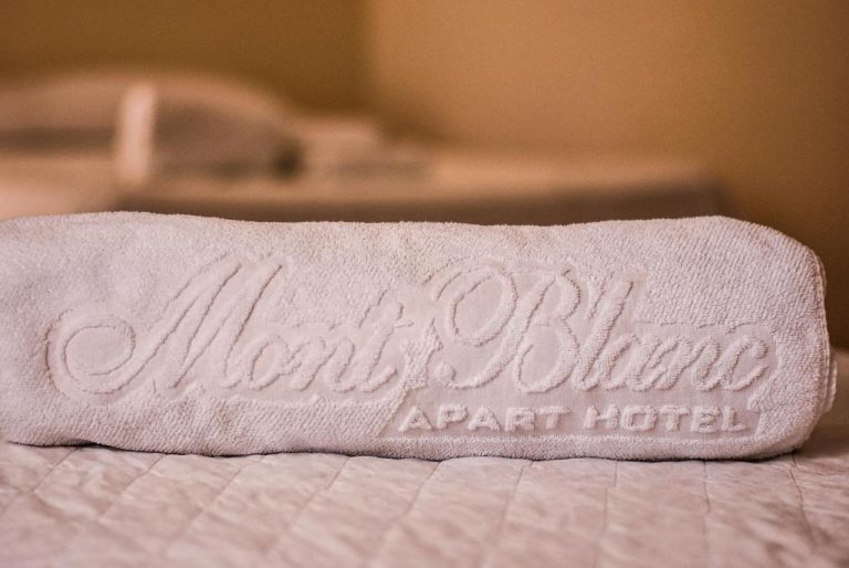 Toalla blanca bordada con el logo del Mont Blanc Apart Hotel Nova Iguaçu sobre cama