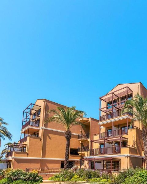 Fachada exterior del Asteria Family Resort Belek con balcones y palmeras bajo cielo azul