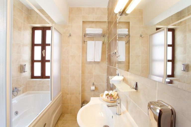 Baño completo con bañera y ducha del Cicerone Lodge Hotel, decorado en tonos beige con toallas blancas