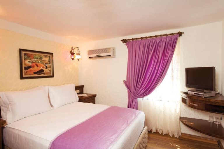 Habitación doble con cama matrimonial y cortinas púrpuras en Cicerone Lodge Hotel