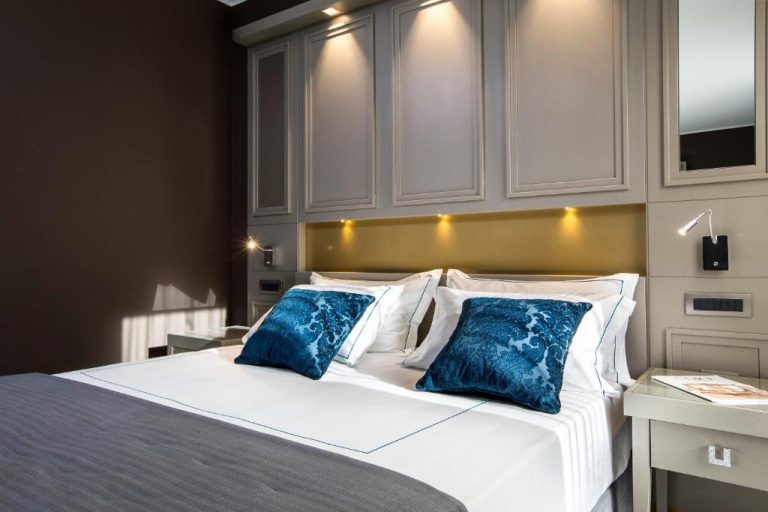 Habitación doble de lujo con cama king y cojines azules en el Palazzo Doglio de Cagliari