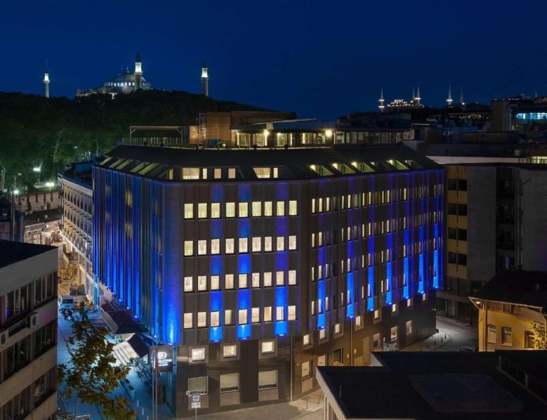Fachada iluminada con luces azules del DoubleTree by Hilton Istanbul Sirkeci con mezquita al fondo