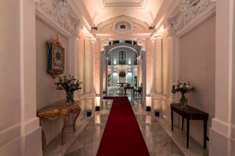 Elegante pasillo de entrada con alfombra roja y decoración barroca en el hotel Domus Zamittello