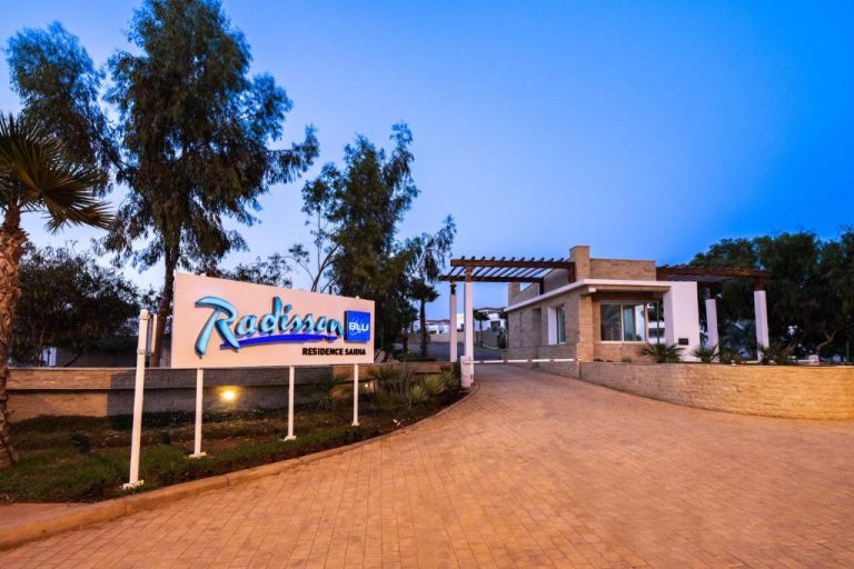 Entrada principal del Radisson Blu Residence Saidia con cartel iluminado y acceso peatonal al atardecer