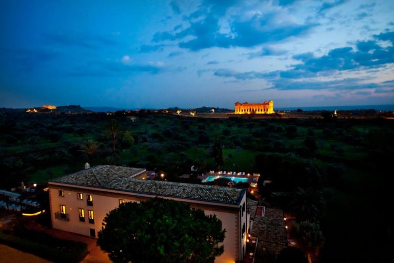 Vista nocturna del Villa Athena Resort con el iluminado Templo de la Concordia en Agrigento al fondo