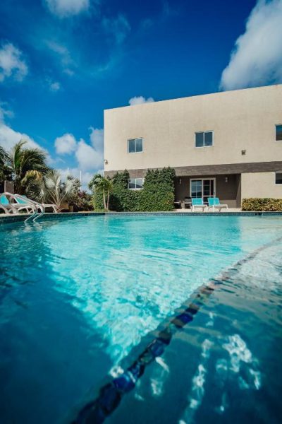 Piscina exterior de aguas cristalinas con tumbonas azules en el Hotel RH Boutique Aruba