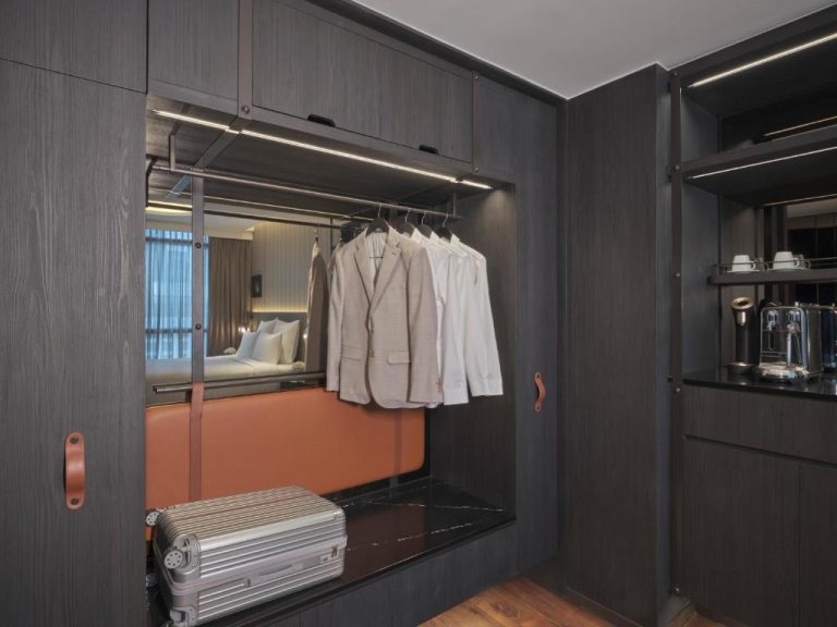 Vestidor de lujo con armario empotrado, maleta Rimowa y trajes colgados en Pullman Singapore Hill Street