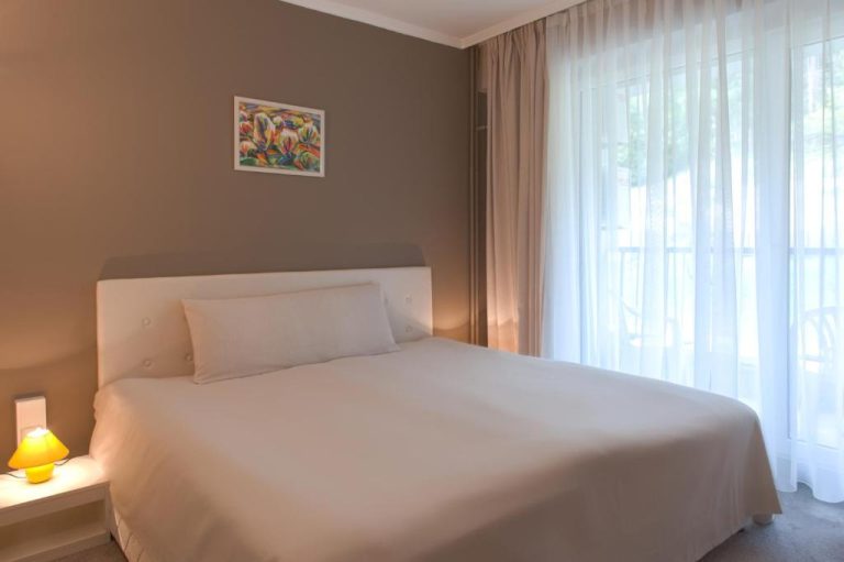 Habitación doble con cama matrimonial blanca y ventanal en Park Hotel Kyustendil Bulgaria