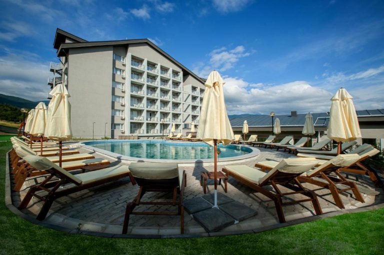 Piscina exterior con tumbonas y sombrillas del Park Hotel Kyustendil rodeada de jardines