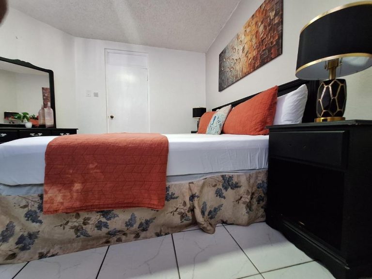 Habitación con cama doble y decoración en tonos naranja en Beach One Bedroom 2, con lámpara elegante y cuadro decorativo