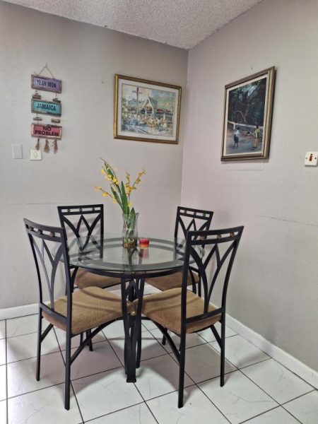 Comedor con mesa redonda de cristal y cuatro sillas en apartamento Beach One Bedroom 2 Jamaica
