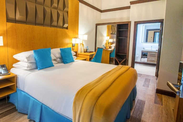 Habitación de lujo con cama doble king size y almohadas azules en Sago Palm Hotel