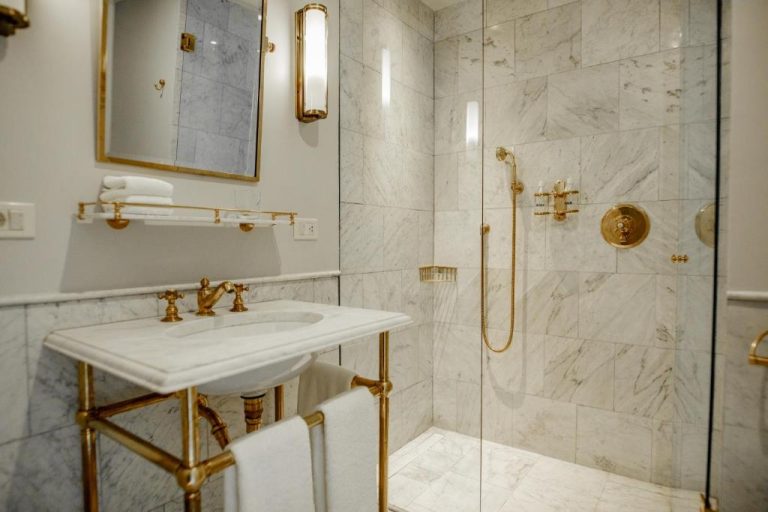 Baño de mármol blanco con griferías doradas y ducha de cristal en Hotel Montevideo Leading Hotels