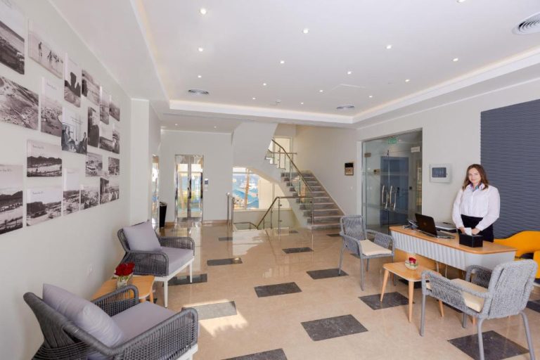 Recepción moderna del Naama Bay Suites & SPA con área de espera, escalera de cristal y fotos históricas en la pared