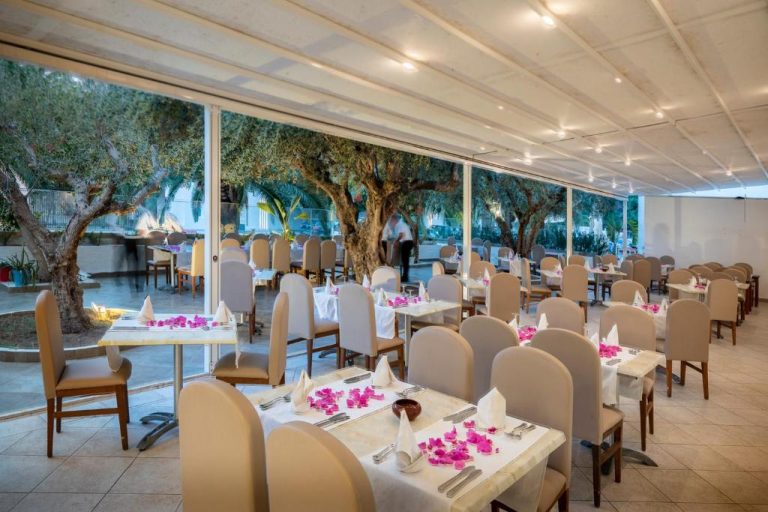 Restaurante interior del Le Hammamet Hôtel & Spa con mesas decoradas con flores rosas y vistas al jardín