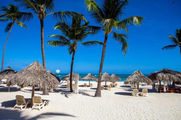 Playa de arena blanca con palmeras y sombrillas de palma en Los Corales Beach Village Punta Cana