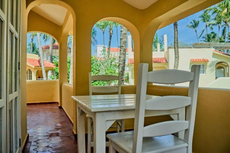 Terraza con mesa y sillas blancas bajo arcos amarillos en Los Corales Beach Village Punta Cana