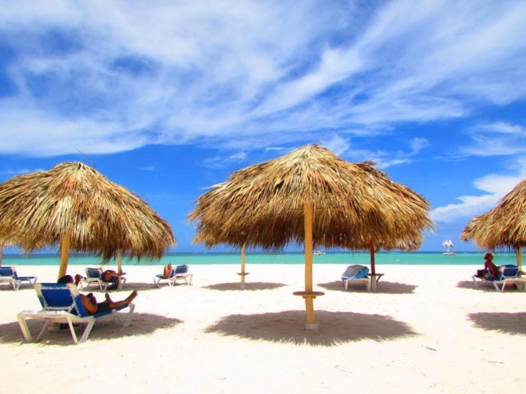 Playa de arena blanca con parasoles de palma y tumbonas en Los Corales Beach Village Punta Cana