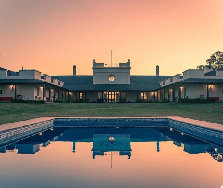 Piscina exterior del Hotel Santa Cristina reflejando el atardecer con vistas a la fachada principal iluminada