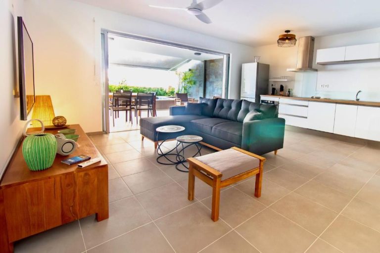 Salón moderno con sofá azul y cocina integrada con terraza exterior en La Plage Martinique