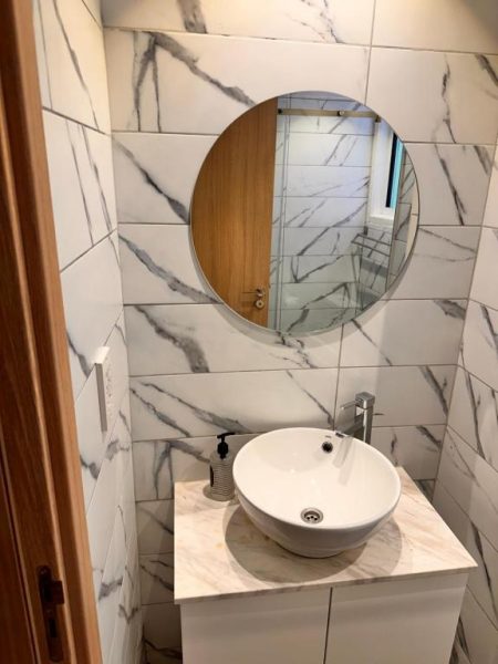 Baño moderno con lavabo sobre encimera de mármol y espejo redondo en San Remo Hotel