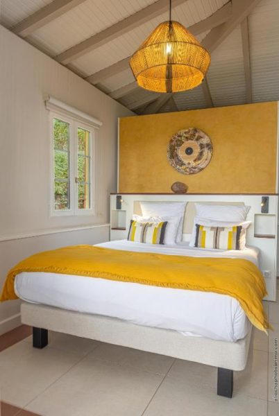 Habitación doble con cabecero amarillo y lámpara de mimbre en La Suite Villa