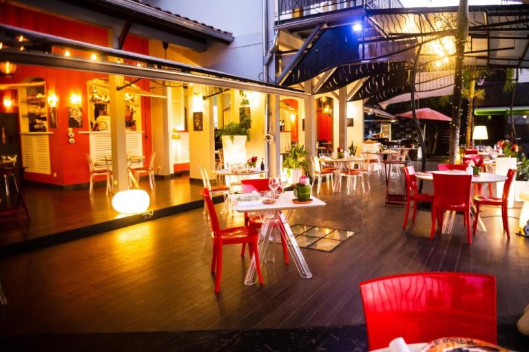Terraza exterior del restaurante La Suite Villa con mesas y sillas rojas iluminadas por la noche