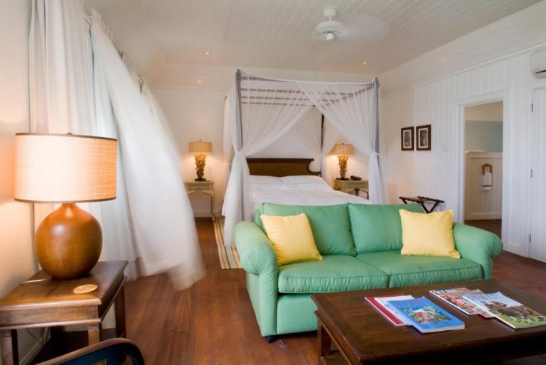 Suite con cama de dosel y sofá verde en The Atlantis Historic Inn, decoración tropical elegante