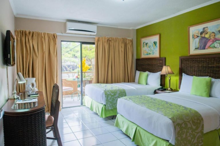 Habitación doble con dos camas y decoración en verde del Aparthotel Guijarros con balcón