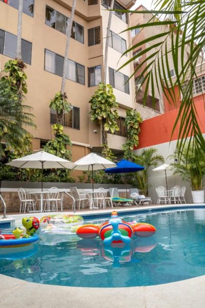 Piscina exterior con flotadores coloridos y zona de descanso del Aparthotel Guijarros rodeada de palmeras