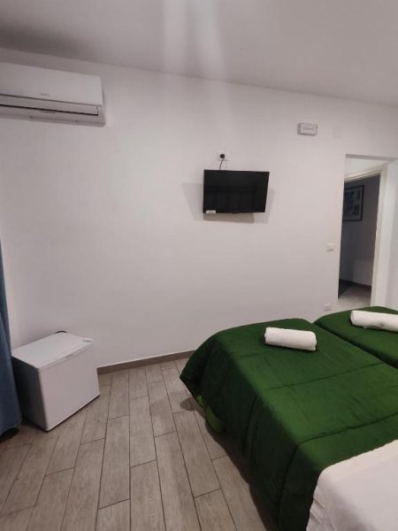 Habitación doble con camas en verde y TV de pared en Hotel Faraglione, con aire acondicionado