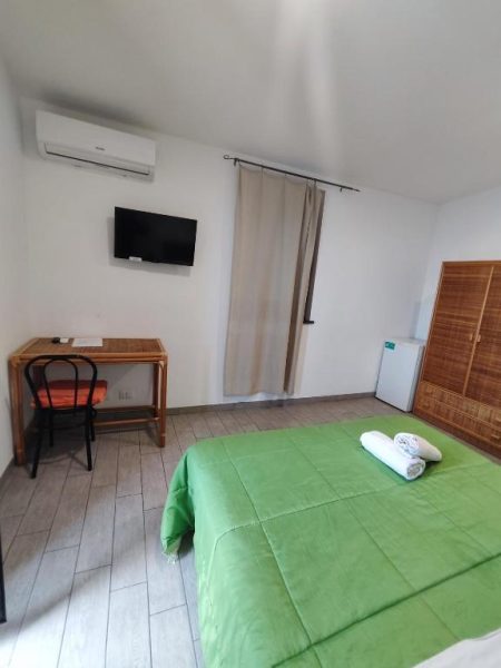 Habitación doble con cama verde y escritorio de madera en Hotel Faraglione